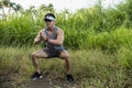 A fit asian male doing bodyweight squats at a grassy field. Working out and training outdoors. Leg workout or calisthenics Royalty Free Stock Photo