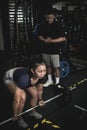 A fit asian woman does conventional barbell deadlifts while her instructor looks on