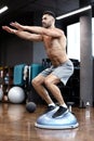 Fit athlete performing exercise on gymnastic hemisphere bosu ball in gym