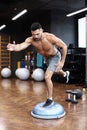 Fit athlete performing exercise on gymnastic hemisphere bosu ball in gym
