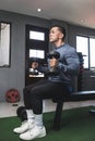 A fit athletic guy in a sweatshirt does seated dumbbell hammer curls. Working out and training biceps. Open air gym setting Royalty Free Stock Photo