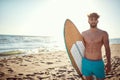 Fit beardy male holding surfboard at the beach, looking away