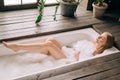 Fit body beautiful blonde young woman taking bath with bubbles in bathroom interior with plenty green plans