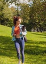 slim fit caucasian woman in colorful fitness outfit walking in the park with yoga mat bottle of watter and smartphone Royalty Free Stock Photo
