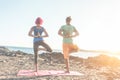 Fit couple doing yoga outdoor on the beach at sunset - Woman and man training on evening time - Tilted horizon composition - Soft