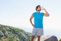 Adult man in sportswear drinking water from reusable bottle on rocky outcrop on coastal trail Royalty Free Stock Photo