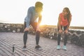 Fit couple taking a rest after fast running workout - Joggers training outdoor at sunset together - Main focus on girl face -