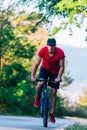 Fit cyclist rides his bicycle bike on an empty road in nature wearing a baseball hat and red t-shirt Royalty Free Stock Photo