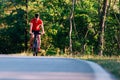 Fit cyclist rides his bicycle bike on an empty road in nature wearing a baseball hat and red t-shirt Royalty Free Stock Photo