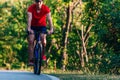 Fit cyclist rides his bicycle bike on an empty road in nature wearing a baseball hat and red t-shirt Royalty Free Stock Photo