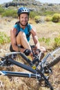 Fit cyclist tying his shoelace on mountain trail smiling at camera