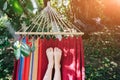 Fit girl is lying in the colourful hammock. Woman with beautiful legs is relaxing in hippie style garden near the village house.