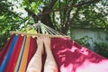 Fit girl is lying in the colourful hammock. Woman with beautiful legs is relaxing in hippie style garden near the village house.