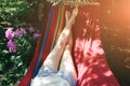 Fit girl is lying in the colourful hammock. Woman with beautiful legs is relaxing in hippie style garden near the village house.