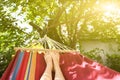 Fit girl is lying in the colourful hammock. Woman with beautiful legs is relaxing in hippie style garden near the village house.