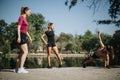 Fit girls enjoying outdoor sports, stretching and warming up in a city park.