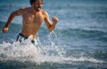 Fit handsome young man running in water at beach. Young sporty man on vacation. Holiday, summertime, fun, sport, recreation, Royalty Free Stock Photo