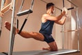 Fit man doing a lunge stretch yoga pilates exercise to strengthen and tone his muscles using a reformer in gym. Health Royalty Free Stock Photo