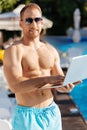 Fit man standing with his laptop near swimming pool