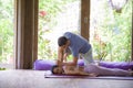 Fit masseur man giving traditional Thai massage to beautiful and relaxed Asian woman lying on studio ground receiving healing