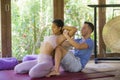 Fit masseur man giving traditional Thai massage to beautiful and relaxed Asian woman lying on studio ground receiving healing