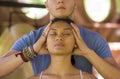 Fit masseur man giving traditional Thai massage to beautiful and relaxed Asian woman lying on studio ground receiving healing