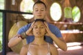 Fit masseur man giving traditional Thai massage to beautiful and relaxed Asian woman lying on studio ground receiving healing