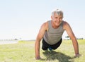 Senior male performing push-ups on grass field wearing grey tank top and blue-accented sneakers Royalty Free Stock Photo