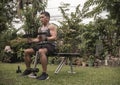 A fit middle aged asian guy prepares to lift seated dumbbell shoulder presses on a bench at his front yard.