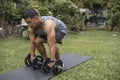 A fit and middle aged asian man is working out outdoors at his lawn, doing dumbbell deadlifts