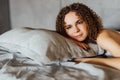 Fit and passionate woman with curly hair laying among bed sheets wearing white lace lingerie and looking seductive and smiling Royalty Free Stock Photo