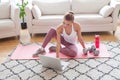 Fit pretty model in activewear sitting on mat using laptop and getting ready for a workout at home Royalty Free Stock Photo