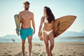 Fit, sexy, young male and female walking and talking on beach, holding surfboards, smiling