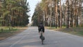 Fit sportive cyclist sprints uphill out of the saddle. Training on road bicycle. Back side follow shot.