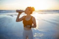 Fit sports woman at beach at sundown drinking water