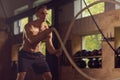 Fit, sporty and athletic sportsman working in a gym. Man training using battle ropes. Cross fit, sports, athletics and