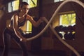 Fit, sporty and athletic sportswoman working in a gym. Woman training using battle ropes. Sports, athletics and fitness