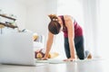 Fit sporty healthy woman on mat in Cat Majaryasana pose, doing breathing exercises, watching online yoga class on laptop computer Royalty Free Stock Photo