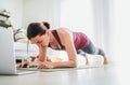 Fit sporty healthy woman on mat in low plank Chaturanga Dandasana yoga pose, doing breathing exercises, watching online yoga class Royalty Free Stock Photo