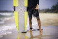 Surfer holds surfboard on the sunny beach showing shaka. Summer holiday hobby Royalty Free Stock Photo