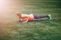 Fit woman in bright sports clothes to do burpees on the green grass