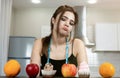 Fit woman with centimeter round neck wearing black sports top standing in the kitchen looking doubtful at cakes and fruits on the Royalty Free Stock Photo