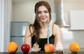 Fit woman with centimeter round neck wearing black sports top standing in the kitchen lookingat cakes and fruits on the table, Royalty Free Stock Photo