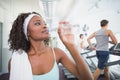 Fit woman drinking water beside treadmills