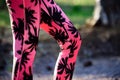 Fit woman in a park during workout, legs detail. Woman wearing pink palm trees pattern fitness leggings.