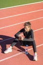 Fit woman resting after workout or running, sitting on a treadmill rubber track, listens to music with wired headphones on Royalty Free Stock Photo