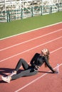 Fit woman resting after workout, sitting on a treadmill rubber track, listens to music with wired headphones on smartphone, taking Royalty Free Stock Photo