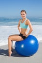 Fit woman sitting on exercise ball at the beach smiling at camera Royalty Free Stock Photo