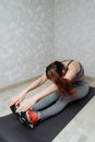 Fit woman stretching her leg to warm up on grey mat at home. Fitness concept, close up on sport shoes