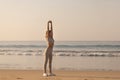 Fit young adult woman in work out clothing stretching hands and body on the beach in the morning Royalty Free Stock Photo